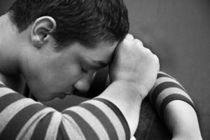 Black and white picture of a young man sitting with his head resting on his fist.